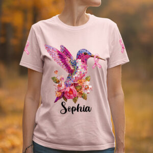 Front lifestyle view of a light pink hummingbird pink ribbon shirt featuring a jeweled bird, flowers, and the name Sophia.