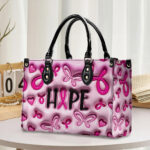 Front view of leather hope pink ribbon handbag featuring 3D butterfly, heart, and text graphics with black handles.