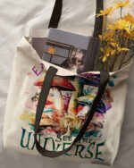 Front view of the eat mushrooms see the universe tote bag featuring vibrant mushroom artwork and sturdy handles.