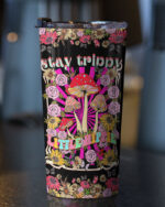 Stay trippy little hippie tumbler featuring vibrant mushrooms and flowers, shown from the front on a dark surface.
