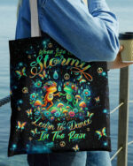 Colorful dance in the rain frog tote bag featuring vibrant frogs and flowers, held by a person outdoors.