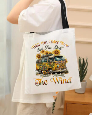 White RUNNING AGAINST THE WIND tote bag featuring a vintage van and sunflowers, shown from the front in casual wear.