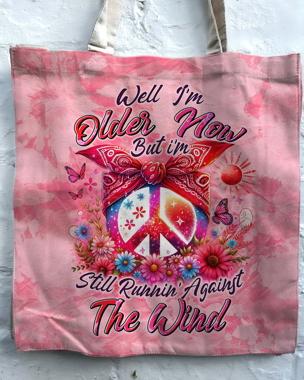 Older Now Running Against The Wind Tote Bag Front view of the older now running against the wind tote bag with vibrant pink color and floral peace sign design.