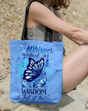 A blue tote bag featuring 'Whisper Words of Wisdom' design with butterflies, shown from the front while being held.
