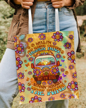 Front view of the colorful older now running against the wind tote bag with floral design and vibrant colors.